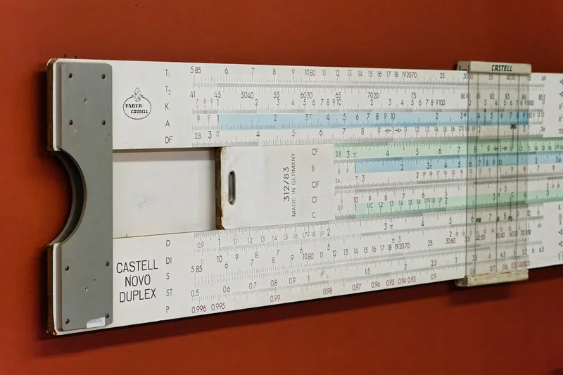 Vintage slide rule from the early 20th century displayed on a wall, showcasing mathematical calculations and engineering design